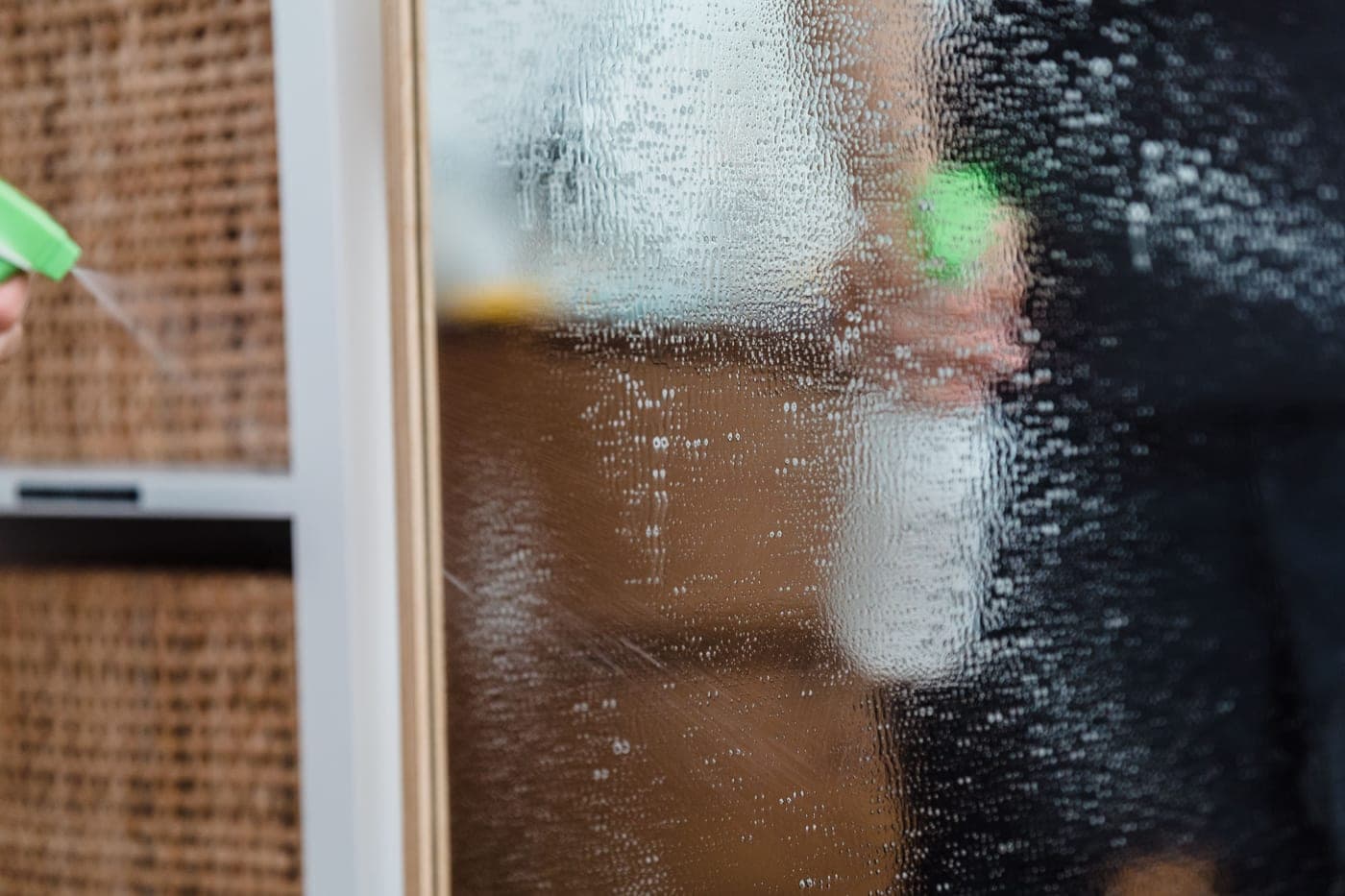 Glass spray bottle and cleaning cloth on a plain counter