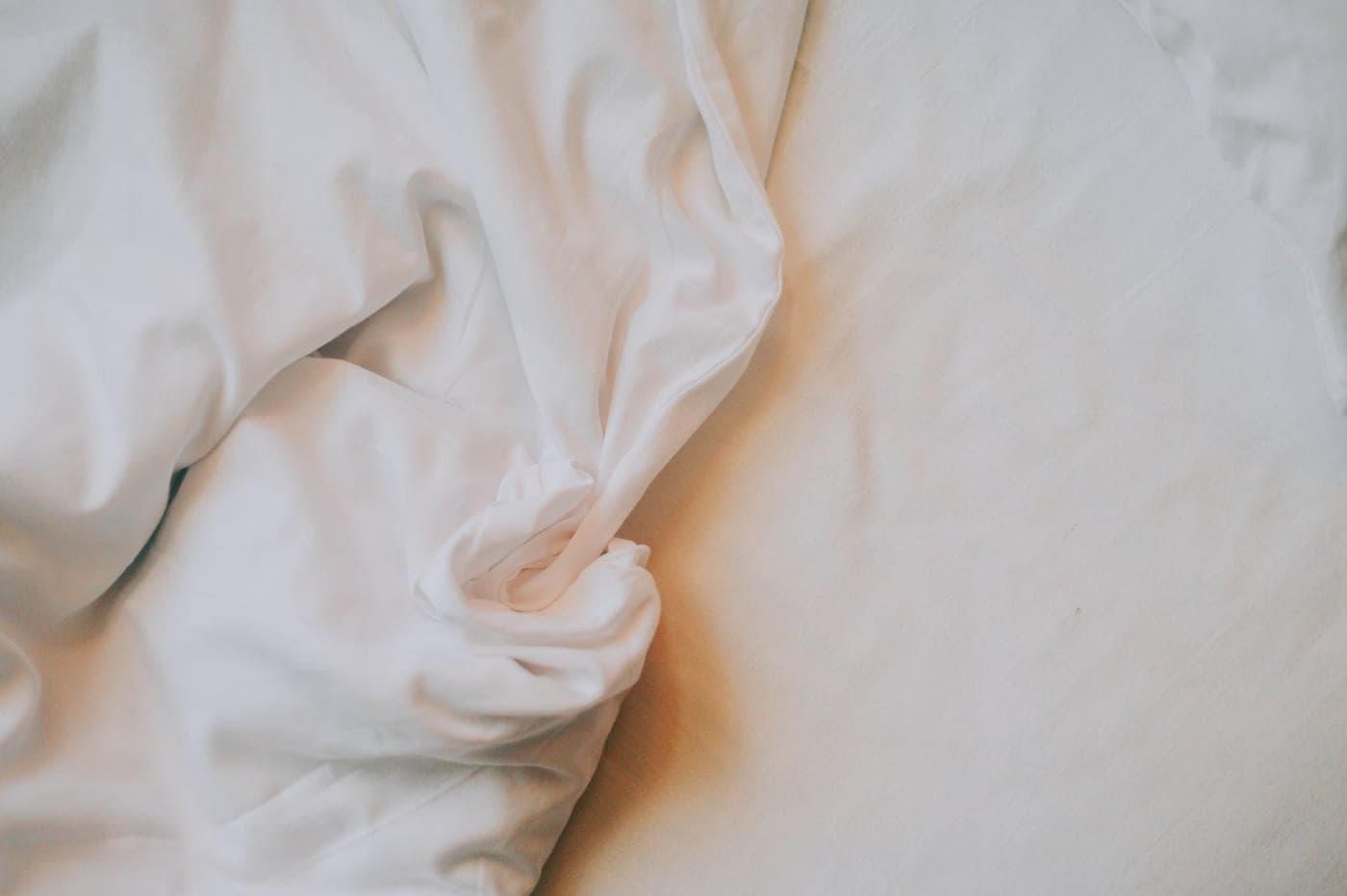 Folded white cotton bed sheets under hard directional light